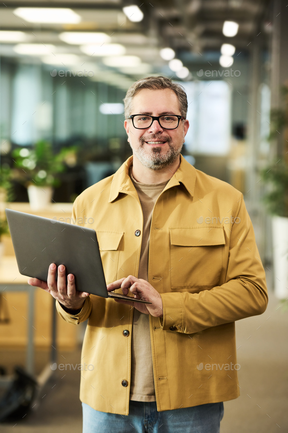 Happy mature chief executive officer with laptop looking at camera - Stock Photo - Images