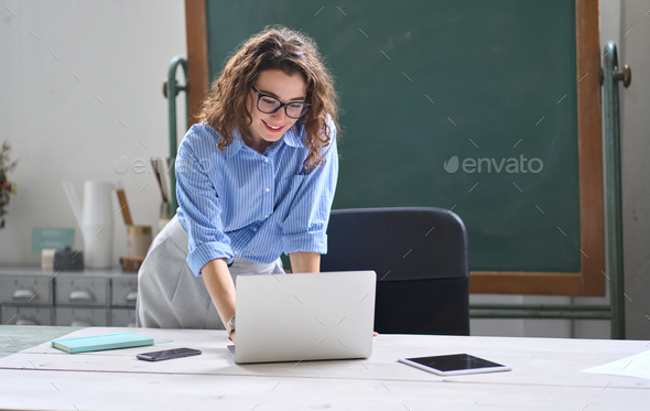 Young woman school teacher, online tutor standing at desk teaching remote class. - Stock Photo - Images