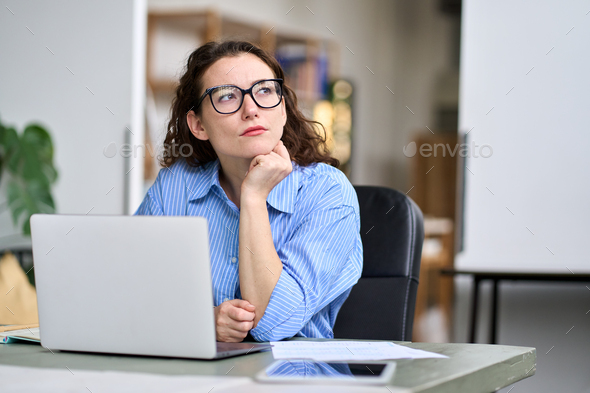 Thoughtful serious professional woman using laptop, looking away thinking. - Stock Photo - Images