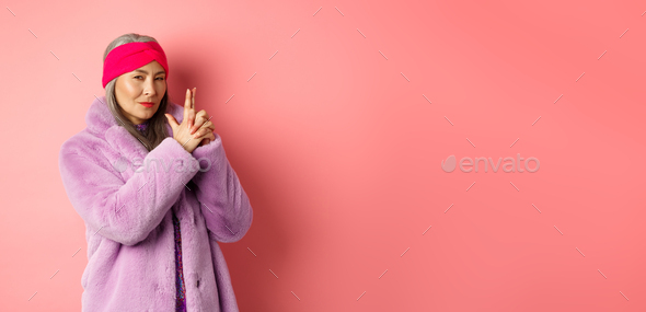 Fashion and shopping concept. Cool and stylish asian old woman in winter coat making finger gun