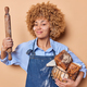 Boastful female baker holds basket of delicious fresh bread and wooden rolling pin demonstrates her - PhotoDune Item for Sale