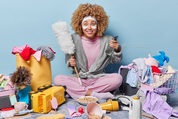 Smiling housewife looks with glad surprised expression holds dusting brush and spraying bottle ready - Stock Photo - Images