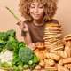 Vertical shot of serious curly haired woman holds asparagus looks with temptation at delicious sweet - PhotoDune Item for Sale
