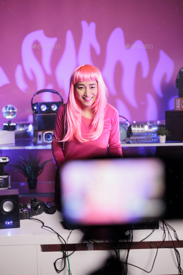 Dj with pink hair performing eletronic song at professional turntables while recording music session