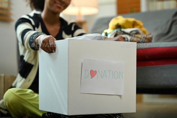 Selective focus on woman hands holding box of clothes with donate label.