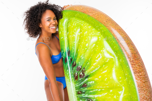 attractive african lady in a blue separate bathing suit holds a kiwi swimming mattress on a white