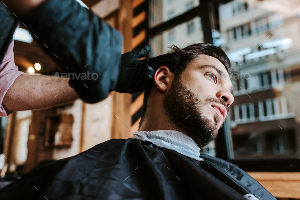 selective focus of barber in latex gloves holding hair comb while styling  hair of man Stock Photo by LightFieldStudios