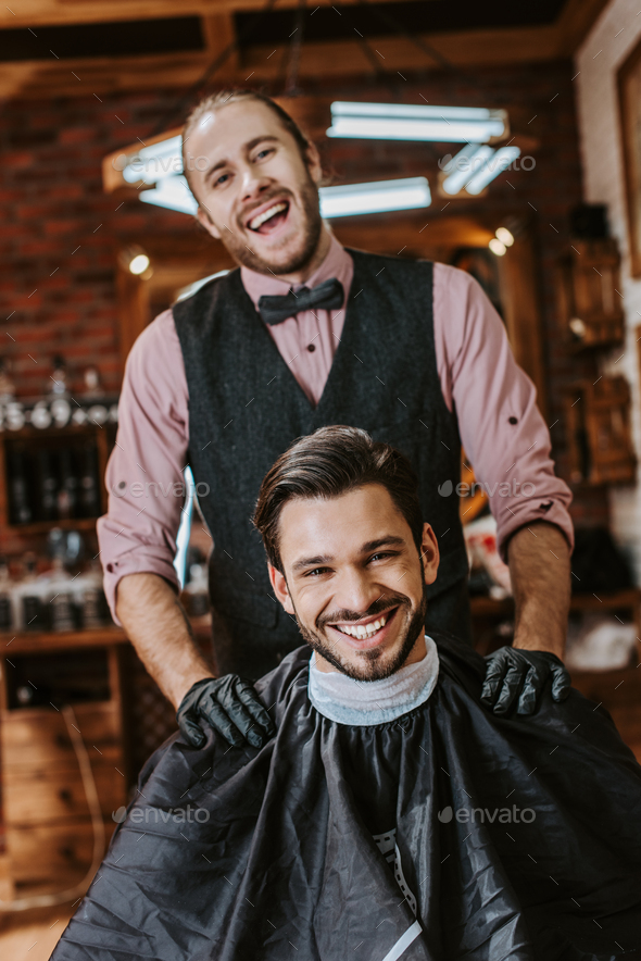 handsome barber in latex gloves putting hands on shoulders of happy man