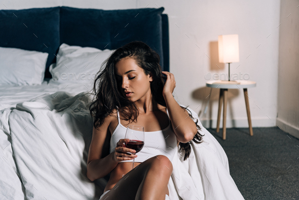 sexy, dreamy girl holding glass of red wine while sitting on floor in  bedroom Stock Photo by LightFieldStudios