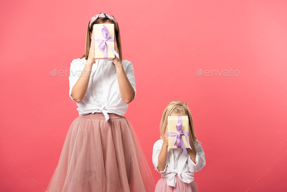 daughter and mother obscuring faces with gifts isolated on pink