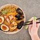 cropped view of woman holding chopsticks near spicy seafood ramen on grey surface - PhotoDune Item for Sale