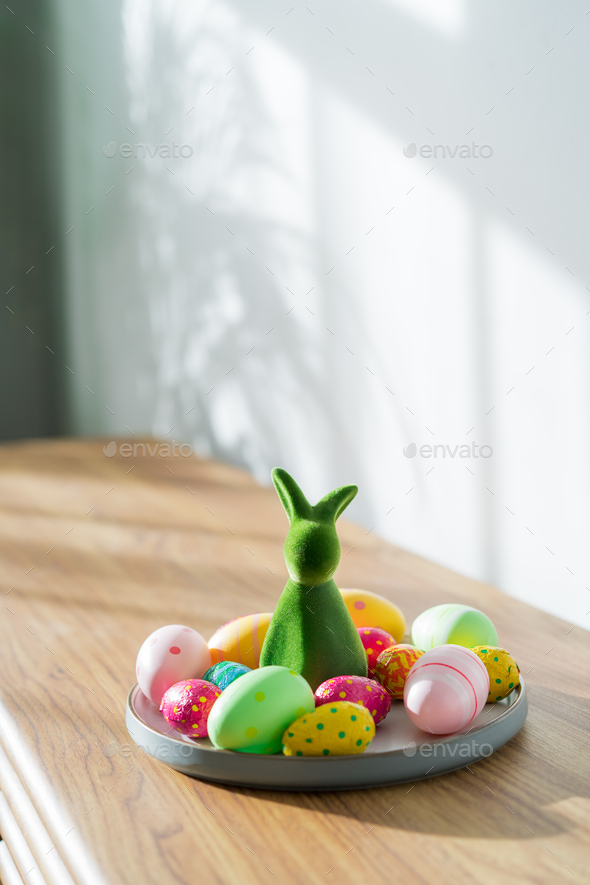 Easter home decor. Composition of Green bunny rabbit figurine and colored easter chocolate eggs