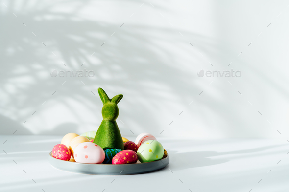 Easter home decor. Composition of Green bunny rabbit figurine and colored easter chocolate eggs