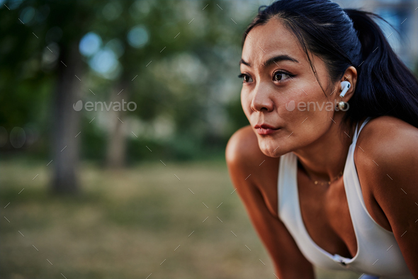 Sporty young woman with bluetooth earphones taking a break after her workout in park