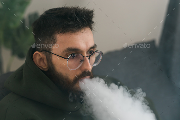 Bearded millennial or gen z man smoking hookah while relaxing on sofa ...