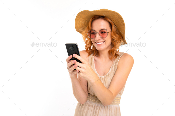 traveler girl in a summer dress with a hat and sunglasses book tickets on a smartphone on a white