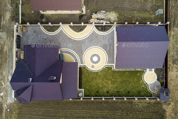 Aerial top view of house shingle roof on background of green lawn and colorful paved yard