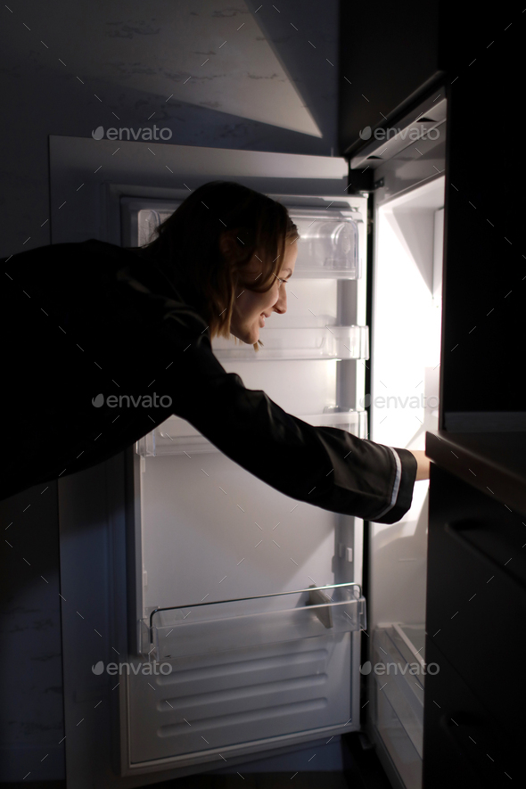 Young woman looking into the fridge looking for food , feeling hungry at night. Night snacking and