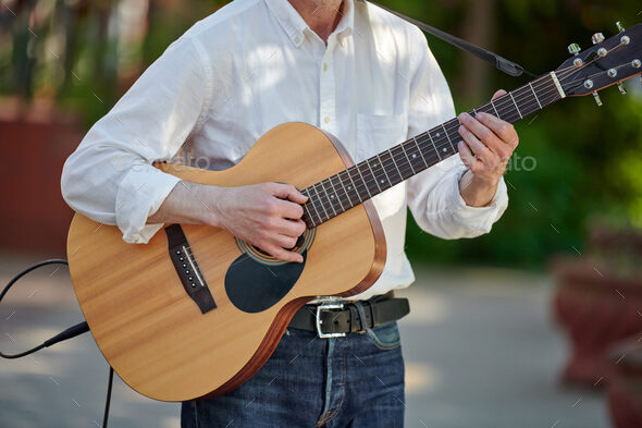 Man playing electro acoustic guitar at outdoor event, free musical performance of street musician