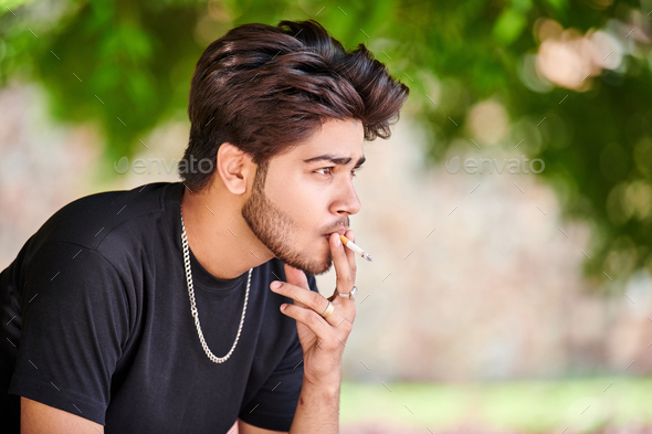 Young indian man smoker portrait in black t shirt and silver neck chain in public park