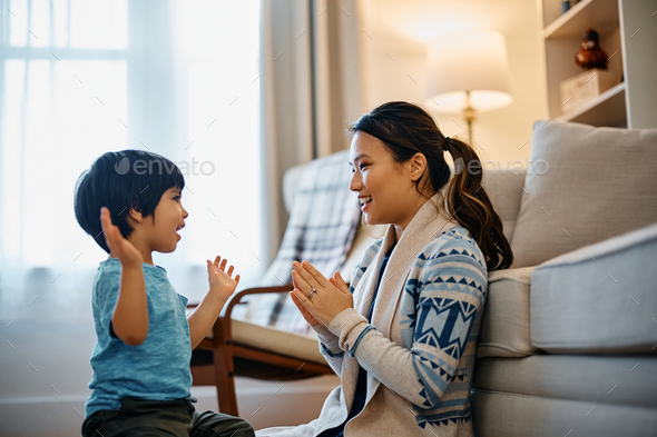 Happy Asian kid and his mother having fun while playing clapping game at home.