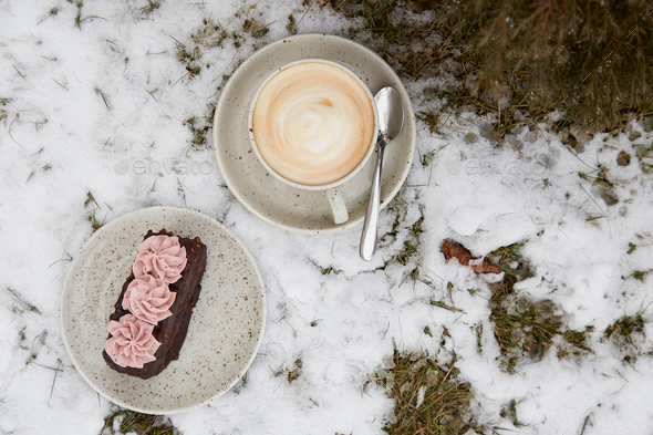 Vegan brownie cake dessert with cup of cappuccino outdoor at the snowy day. Coffee with dessert.