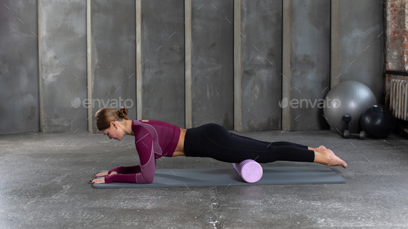 A young woman in sportswear performs a myofascial hip massage with a roller. Muscle recovery, mfr.