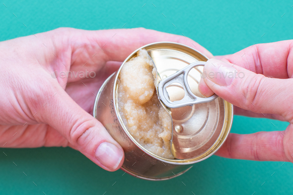 The hand of an adult man holds a can of canned food, the second hand opens the lid jerking a key