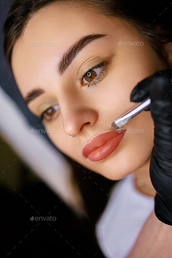 Applying foundation with a brush around the lip contour after permanent makeup.