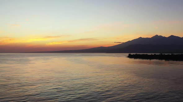 Yellow clouds on bright sky after sunset reflecting on calm surface of seawater around silhouette of alt