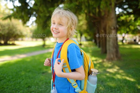 Elementary boy with backpack, bottle of water and name badge on his neck goes to school