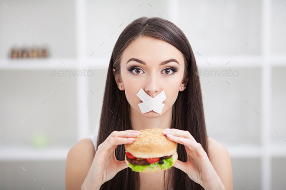 Young woman with duct tape over her mouth, preventing her to eat junk food