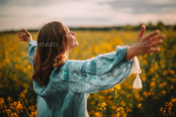 Happy free ukrainian woman in embroidery blouse in yellow canola field.Open arms