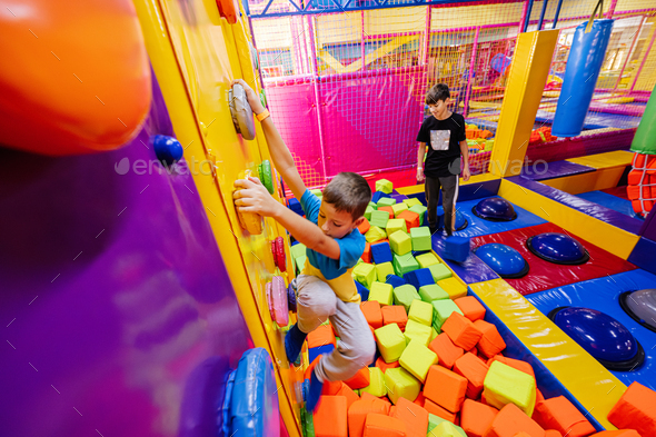 Happy kids playing at indoor play center playground, brothers climbs in  wall. Stock Photo by ASphotostudio