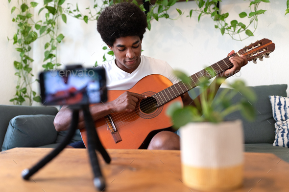 African American guitar teacher filming himself with phone showing students how to play.
