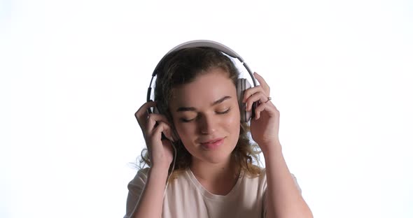 Happy Woman Putting on Headphones Listening To Music and Dancing on White Isolated Background