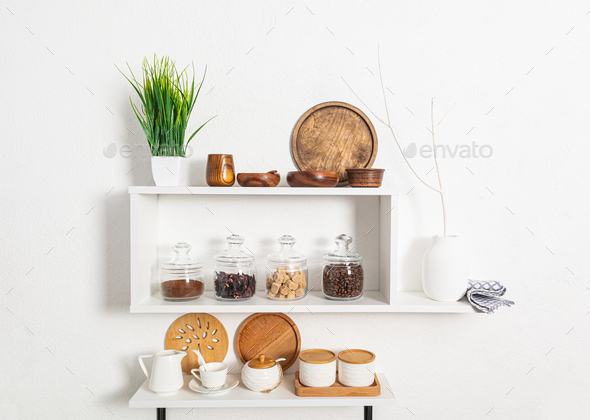 a set of wooden and ceramic dishes, glass filled jars with bulk products on kitchen shelves on wall.