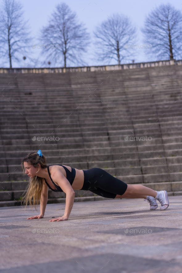 Caucasian young woman doing fitness in a city park, isometric crunches or stabilization