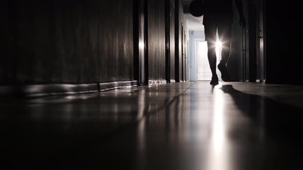 Silhouette of Man Dribbling Basketball and Going along Hallway