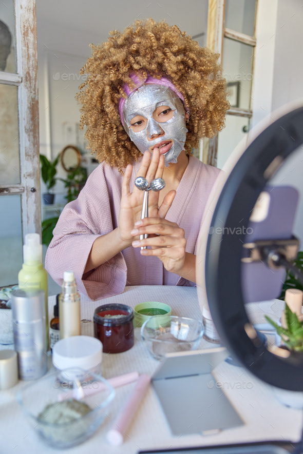 Charming serious curly female vlogger makes photo for blog advertises new beauty products records