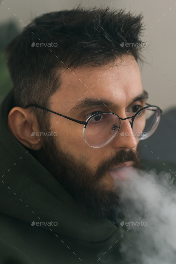Bearded millennial or gen z man smoking hookah while relaxing on sofa