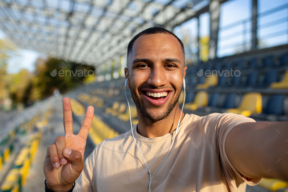 Sportsman runner in stadium taking selfie photo and talking on video call with friends, hispanic