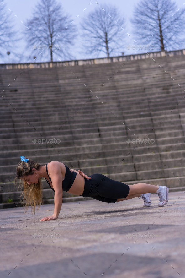Caucasian young woman doing fitness in a city park, isometric crunches or stabilization