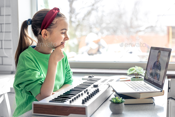 A girl learns to play the piano with a teacher online, remote learning music.