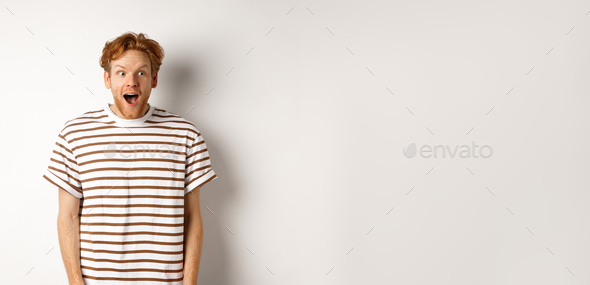 Special promotion concept. Amazed redhead male model gasping, staring at logo or promo offer with