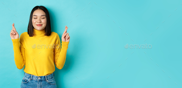 Portrait of hopeful asian girl dreaming about wish come true, cross fingers for good luck and