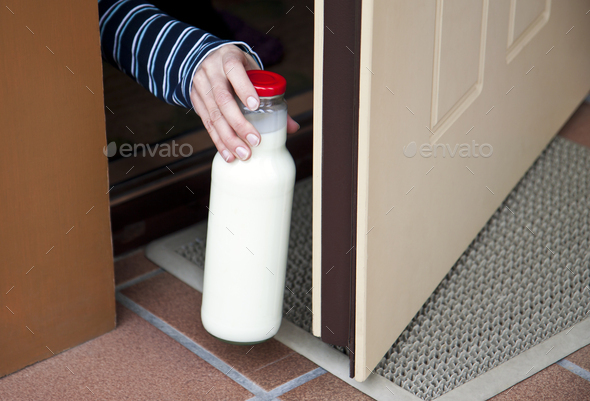 Human hand picking a bottle of milk at doorstep