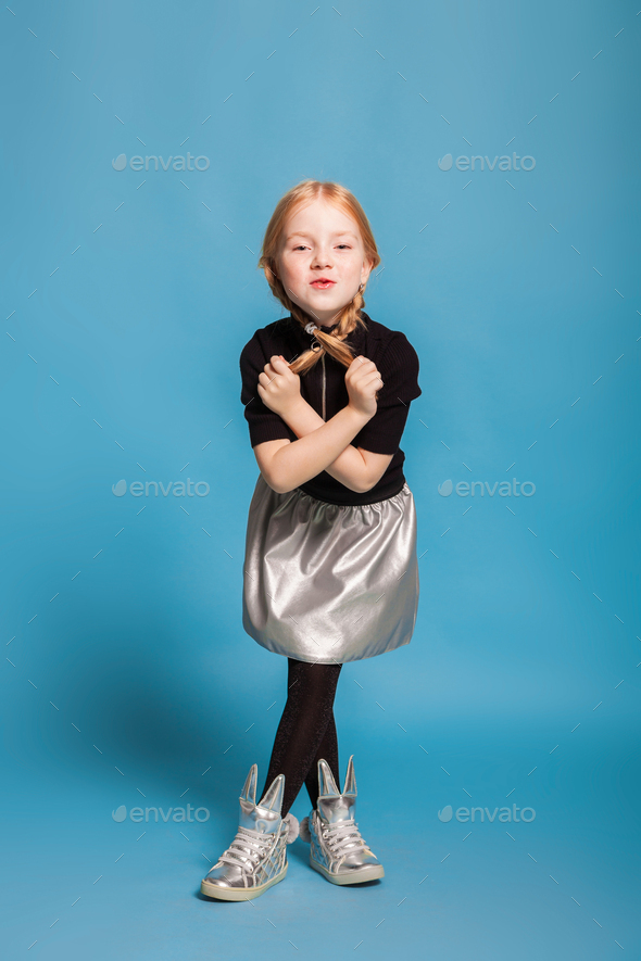 little girl with braids in stylish clothes on blue background