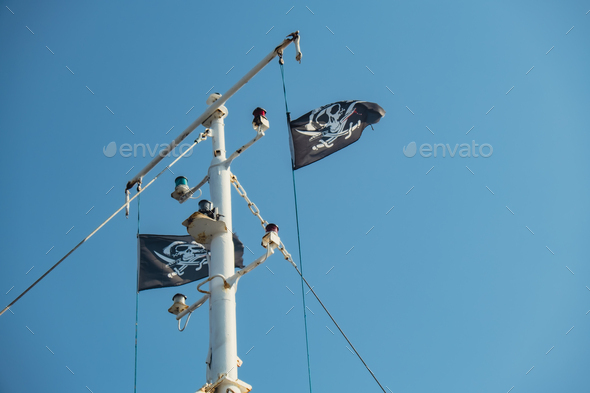 Jolly Roger or pirate ship flag waving with flagpole and blue sky, skull and crossbones, Pirates of