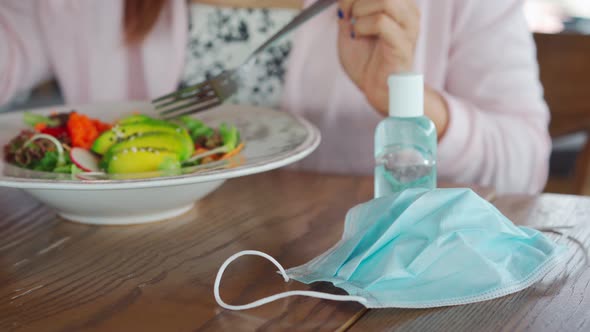 Young woman using alcohol gel sanitizer before meals in restaurant